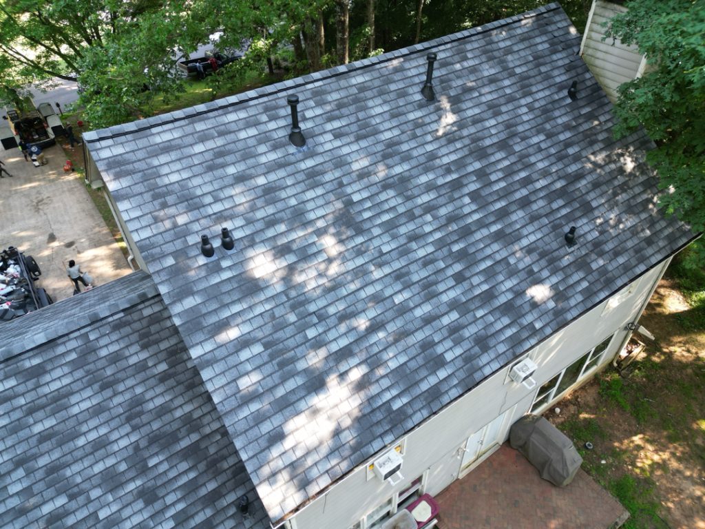 Aerial view of a gray shingled roof with vents, surrounded by trees and a driveway.